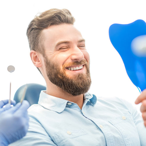 Junger Mann mit Vollbart lächelt nach der Zahnbehandlung.