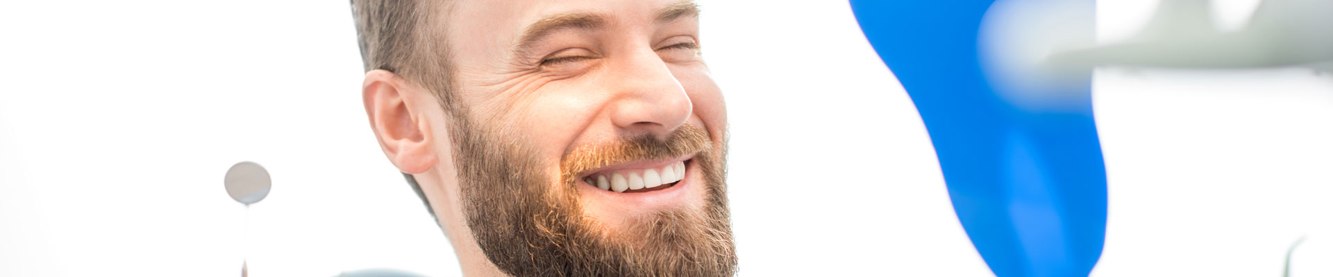 Junger Mann mit Bart zeigt ein schönes Lächeln in der Zahnarztpraxis